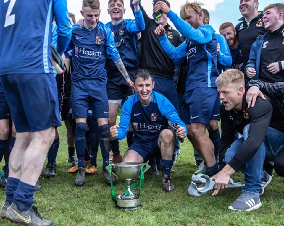 Rosemount Senior Men's team  surrounding a trophy. They are all dressed in blue strip and celebrating a win.celebrating